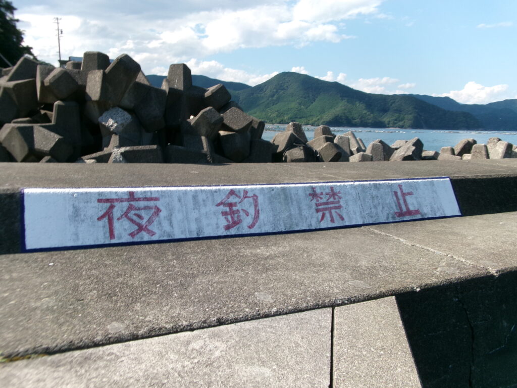 2025年8月20日の現地調査時の夜釣り禁止と書かれた堤防の写真。奥にはテトラポットが写っている。